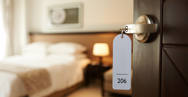 Hotel room door ajar with the bed in the background a a key with the room number hanging from the tag